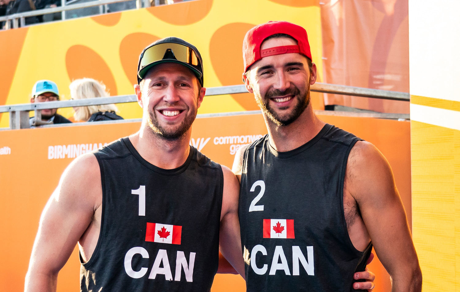 Sam and Dan from the canadian beach volleyball team wearing canada shirts in front of orange background