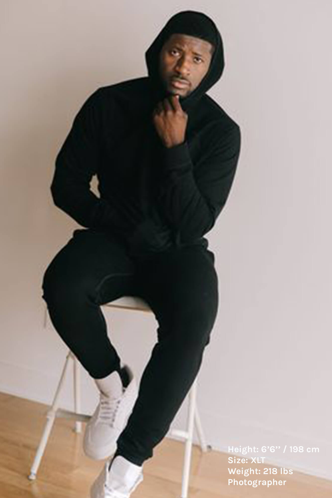 tall guy wearing navy or black hooded sweatshirt and pants sat on stool in studio