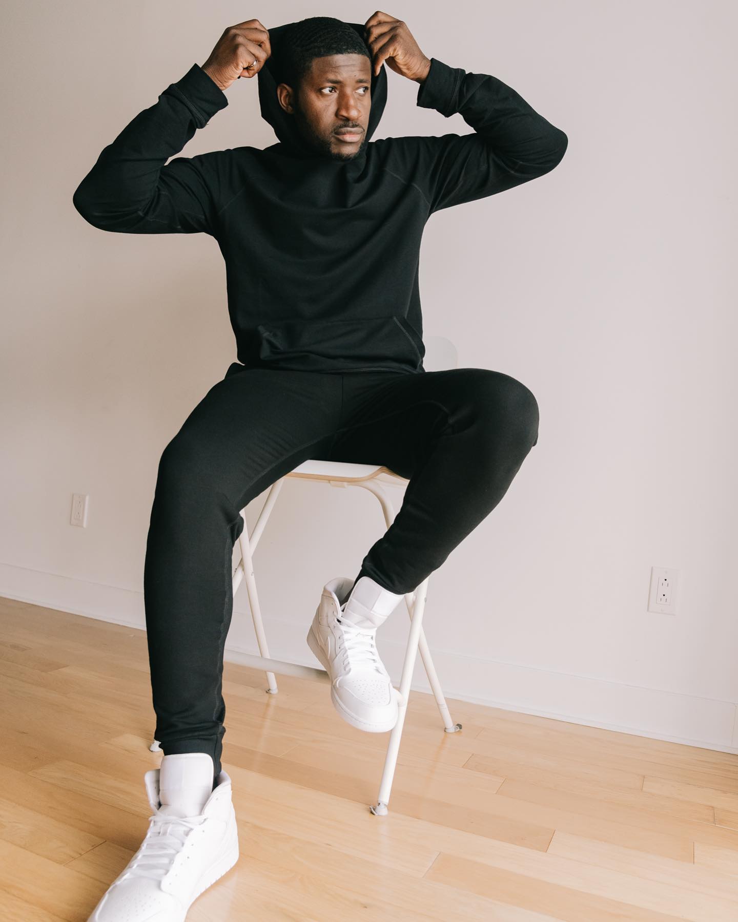 tall guy with dark hair sat on white chair wearing black shirt and joggers