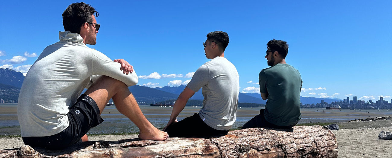 3 men sat on logo wearing sports clothing on jericho beach in vancouver