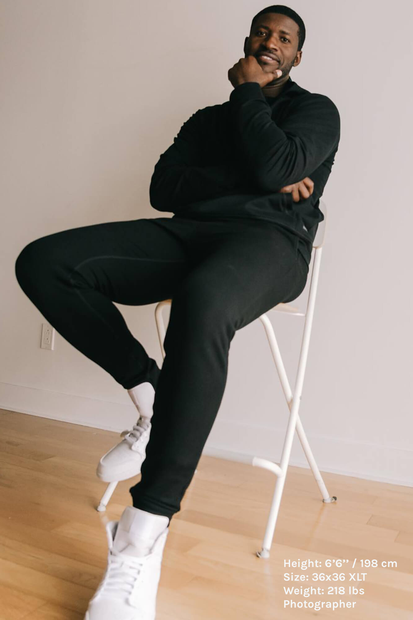 tall guy with dark hair sat on white chair wearing black shirt and joggers