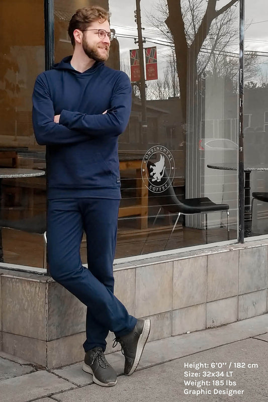 tall man with glasses wearing blue navas lab hoodie and panrs. He is leaning against a window