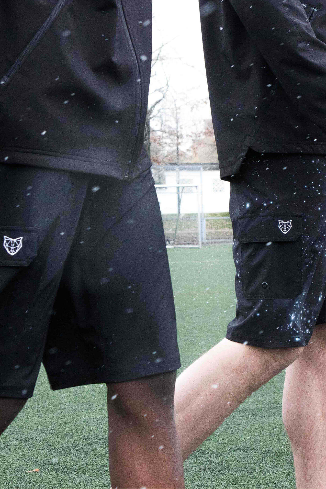 close up of two tall men wearing black navas lab boardshorts on soccer pitch