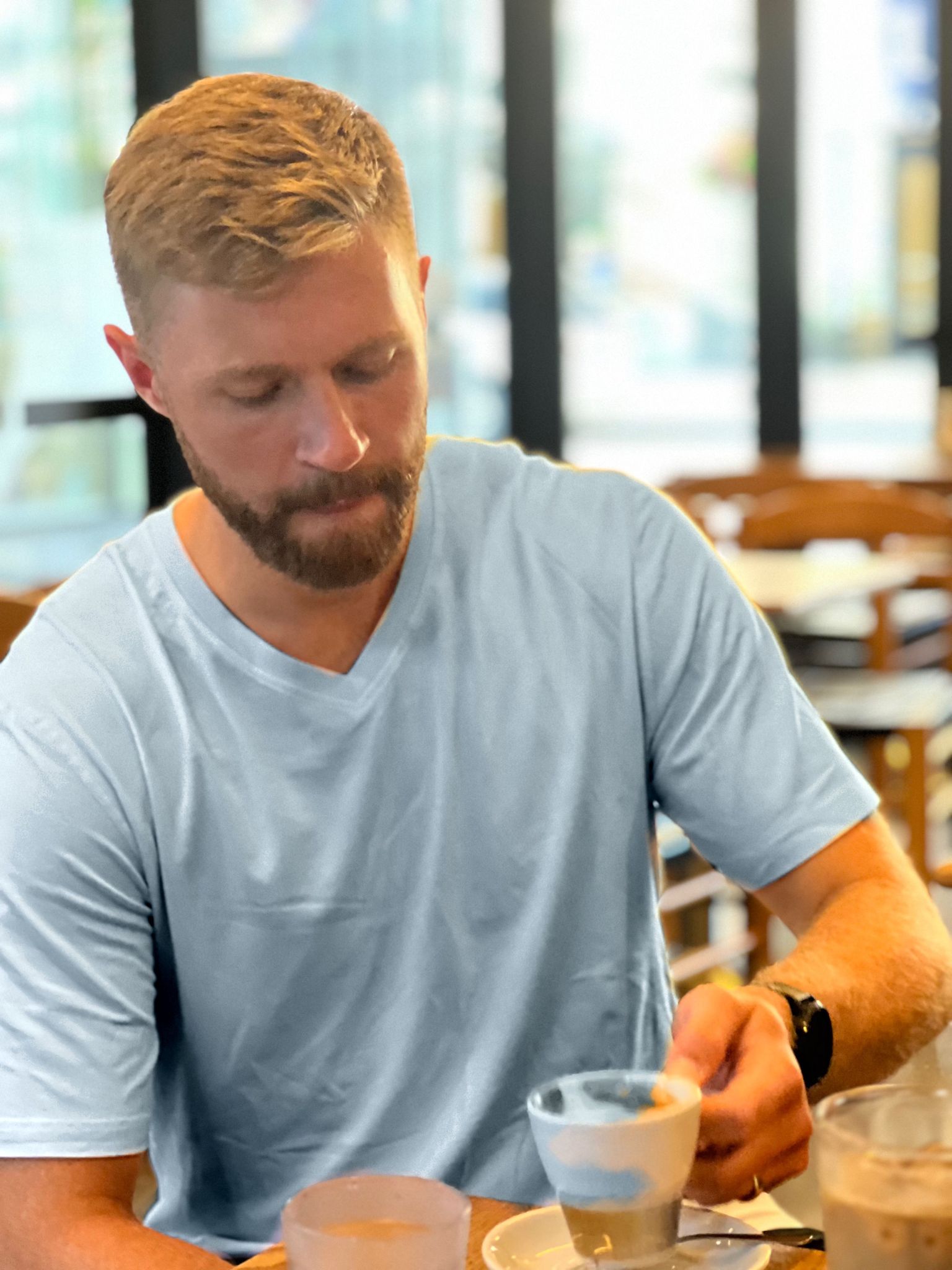 tall blond guy with beard wearing blue navas lab v-neck tee drinking espresso in coffee shop