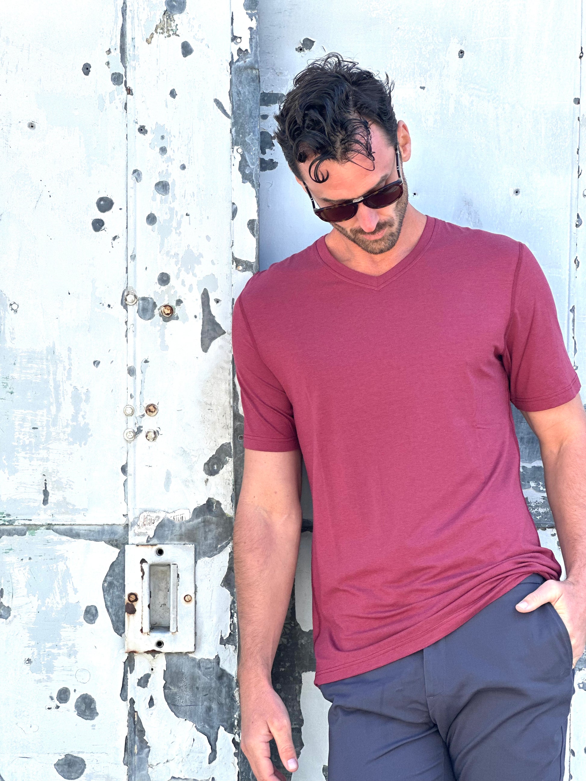 tall male wearing red navas lab v-neck tee stood next to grey wall